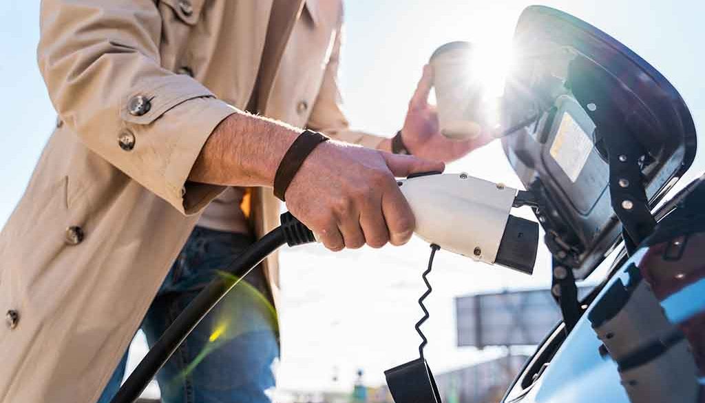 Stylish man inserts plug of the charger into the socket of electric car close-up