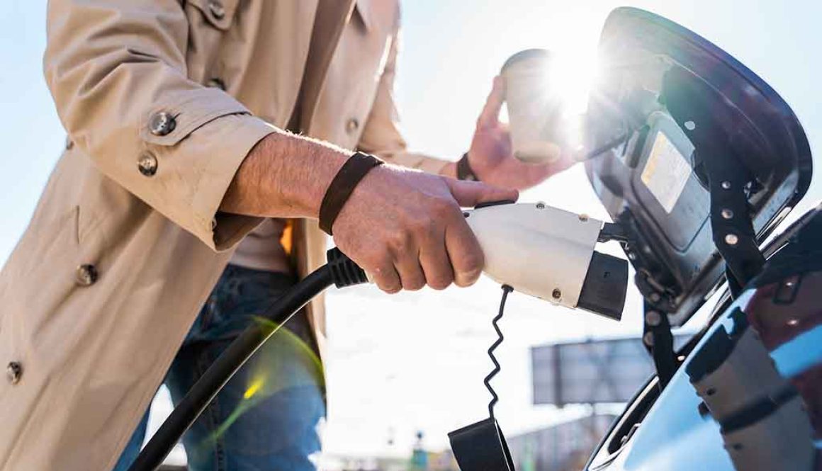 Stylish man inserts plug of the charger into the socket of electric car close-up