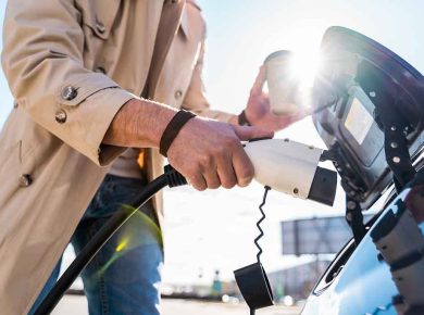 Stylish man inserts plug of the charger into the socket of electric car close-up